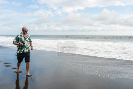 Téléchargez les photos : Photo avec espace de copie d'un homme marchant le long d'une plage de sable avec une caméra - en image libre de droit