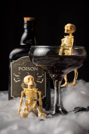 Téléchargez les photos : Verre de veuve noire cocktail d'Halloween avec squelette et bouteille de poison sur toile d'araignée, fond noir, vertical - en image libre de droit