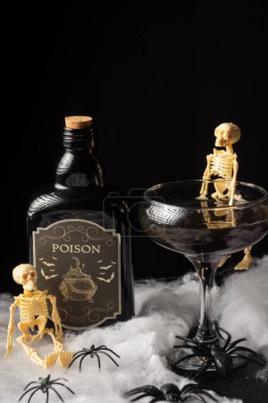 Téléchargez les photos : Vue du dessus du verre à cocktail noir Halloween avec squelettes et bouteille de poison sur toile d'araignée, fond noir, vertical - en image libre de droit