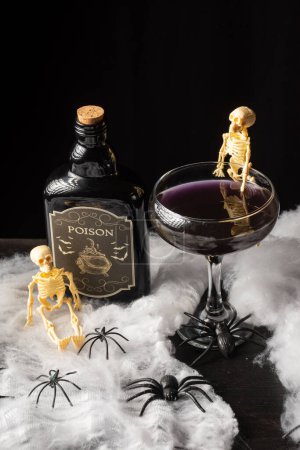 Téléchargez les photos : Vue du dessus du verre à cocktail Halloween avec squelettes et bouteille de poison sur toile d'araignée, fond noir, vertical - en image libre de droit