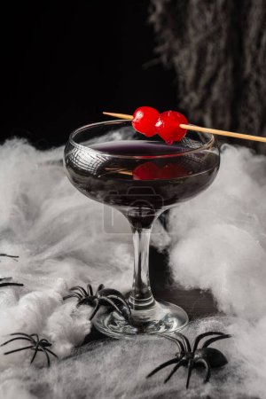 Téléchargez les photos : Vue du dessus du verre de cocktail Halloween veuve noire avec cerises rouges et araignées sur toile d'araignée, fond noir, vertical - en image libre de droit