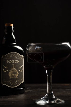 Téléchargez les photos : Gros plan du verre à cocktail Halloween veuve noire avec bouteille empoisonnée, mise au point sélective, sur table en bois sombre, fond noir, vertical - en image libre de droit