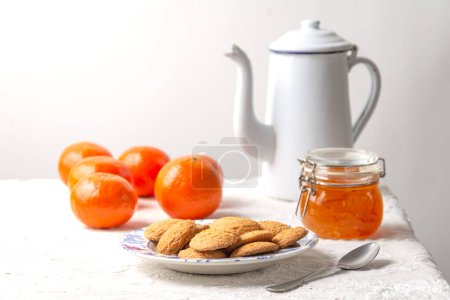 Photo for Still life view of biscuits, old coffee pot, jam, spoon and tangerines on white tablecloth, white background, horizontal with copy space - Royalty Free Image