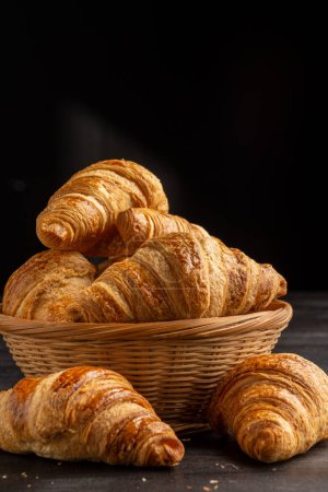 Photo for Close-up of croissants in basket on board on dark wooden table with crumbs, selective focus, black background, vertical, with copy space - Royalty Free Image