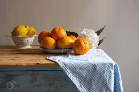 View of still life with citrus fruits on rustic wooden table with checkered cloth and flowers, white background, horizontal with copy space