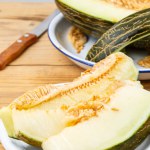 Close-up of green melon slices in white plate on wooden table, with half a melon, selective focus, vertical, with copy space