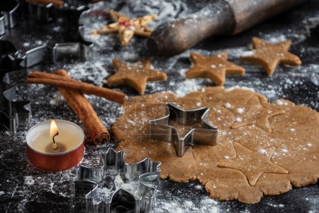Photo for Close-up of gingerbread cookie dough with stars on wooden table with candle, flour and rolling pin, horizontal - Royalty Free Image