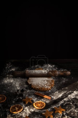 Photo for Top view of dark table with gingerbread cookie dough with rolling pin, flour and molds, black background, vertical, with copy space - Royalty Free Image