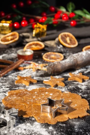 Photo for Close-up of gingerbread cookie dough for Christmas with star molds, cinnamon and oranges on dark table with flour, vertical - Royalty Free Image
