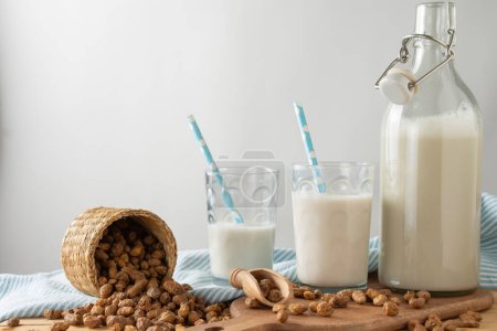 Close-up of two glasses and bottle with horchata on table with tiger nuts and kitchen towel, white background, horizontal, with copy space