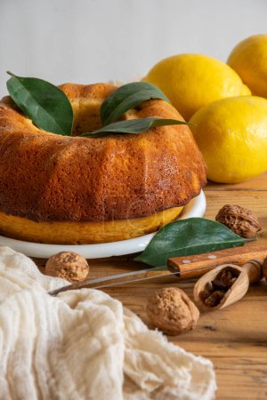 Closeup of table with lemon bundt, walnuts, lemons, knife and rag, white background, vertical, with copy space