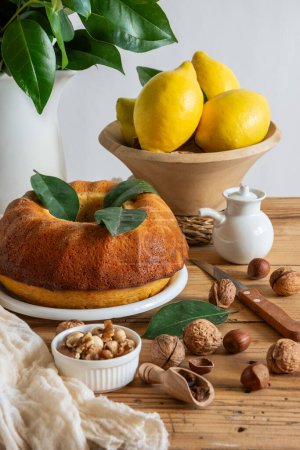 Top view of lemon bundt, walnuts, hazelnuts, lemons, knife and rag, white background, vertical, with copy space
