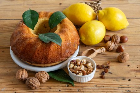 Top view of rustic table with lemon bundt, walnuts, hazelnuts, raisins and lemons horizontally, with copy space