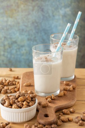 Top view of two glasses of horchata with cinnamon and blue straws on wooden table and board with tiger nuts, gray background, vertical, with copy space