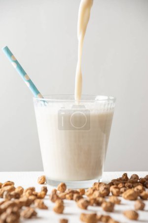 Close-up of horchata in glass with blue straw on white table with tiger nuts, white background, vertical, with copy space
