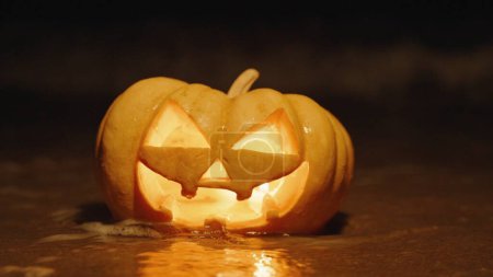 Halloween pumpkin on the seashore, a wave covers it and extinguishes the candles inside, close-up