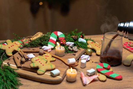 Téléchargez les photos : Ambiance de Noël avec biscuits au pain d'épice et bougies sur la table, verser du chocolat chaud à partir d'un thermos. - en image libre de droit