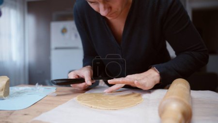 Téléchargez les photos : Une jeune femme prépare des biscuits au pain d'épice pour Noël. Elle place des pochoirs sur la pâte et découpe des formes de canne à sucre. - en image libre de droit