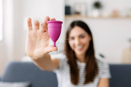 Foto de Smiling young adult woman showing silicon reusable menstrual cup. Focus on foreground - Imagen libre de derechos