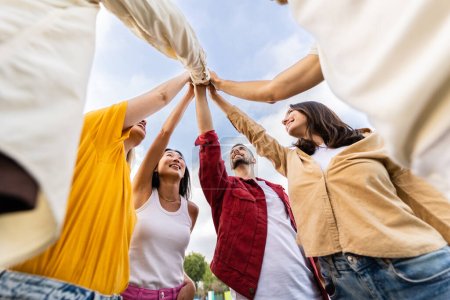 Photo for Young group of happy people stacking hands outside. Diverse community of student friends showing unity celebrating together outdoors. - Royalty Free Image