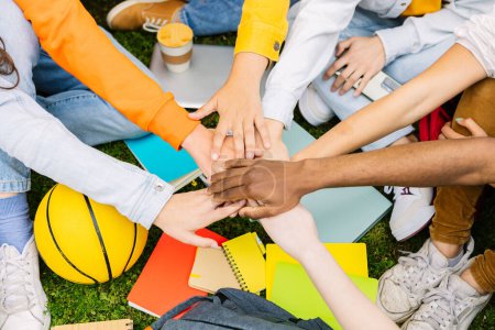 Photo for Diverse student people stacking hands together sitting outdoors at college campus. Youth community concept with young group of millennial students joining hands together showing unity and oneness. - Royalty Free Image