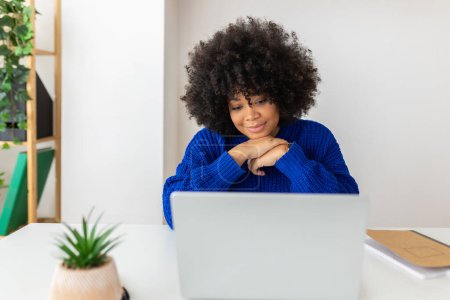 Téléchargez les photos : Jeune femme afro-américaine travaillant sur un ordinateur portable. Femme d'affaires concentrée regardant l'écran d'ordinateur lisant un article d'emploi ou écoutant à la classe virtuelle de formation d'appel vidéo. Concept d'entreprise - en image libre de droit