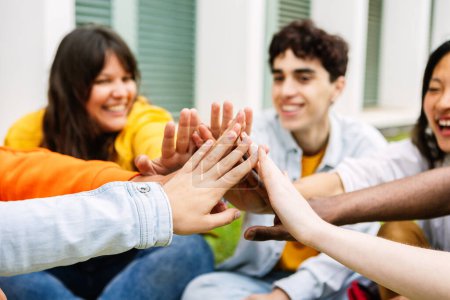Photo for Diverse group of student friends joining hand showing unity and support sitting together at university campus grass. - Royalty Free Image