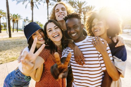Portrait group of young multicultural trendy friends looking at camera while standing by palm trees background. Outdoor photo of diverse happy people having fun in summer. Focus on black guy