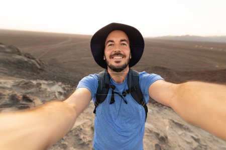 Happy tourist taking selfie over desert landscape during vacation. Joyful traveler male enjoying discovery trip. Travel and adventure concept.