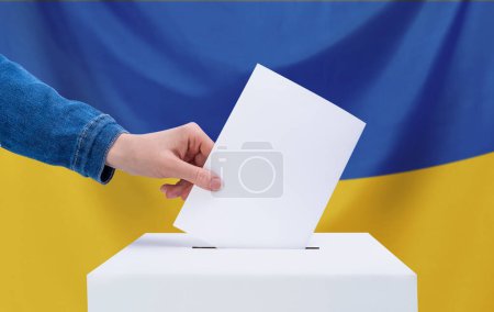 Das Konzept der Wahlen. Eine menschliche Hand wirft einen Stimmzettel in die Wahlurne. Wahlen, Ukraine. Die Flagge der Ukraine im Hintergrund.