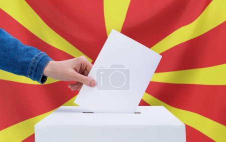 Elections, North Macedonia. Election concept. A hand throws a ballot into the ballot box. Flag of North Macedonia on background.