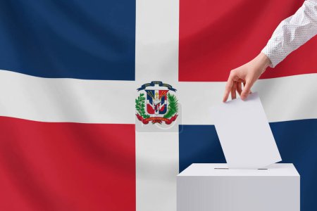 Der Wähler wirft den Stimmzettel in die Urne. Wahlen, Dominikanische Republik. Dominikanische Republik Flagge im Hintergrund.