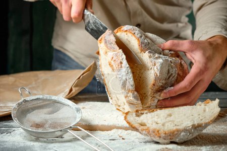 Mann schneidet frisches Brot auf Holztisch