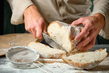 Mann schneidet frisches Brot auf Holztisch