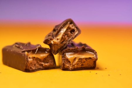 Appetizing broken chocolate bar with caramel and nuts on a bright background