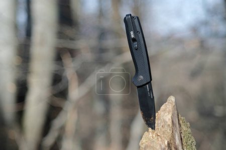 Foto de LVIV, UCRANIA - 27 de febrero de 2024: SOG Terminus cuchillo negro en el bosque sobre un fondo de madera. - Imagen libre de derechos