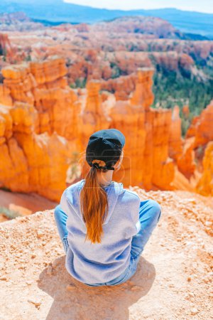 Hiker girl in Bryce Canyon resting enjoying view in beautiful nature landscape with hoodoos, pinnacles and spires rock formations. Bryce Canyon National Park landscape in Utah, United States. 
