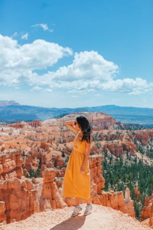 Foto de Caminante mujer en vestido amarillo senderismo con una vista increíble de hoodoos, pináculos y agujas formaciones rocosas en el Parque Nacional Bryce Canyon, Utah - Imagen libre de derechos