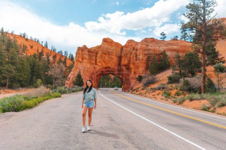 Foto de Joven mujer feliz en el fondo del arco de piedra natural Puente en el Parque Nacional del Cañón Rojo en Utah, EE.UU.. Arco de piedra natural en Red Canyon, Dixie National Forest, Utah, Estados Unidos - Imagen libre de derechos