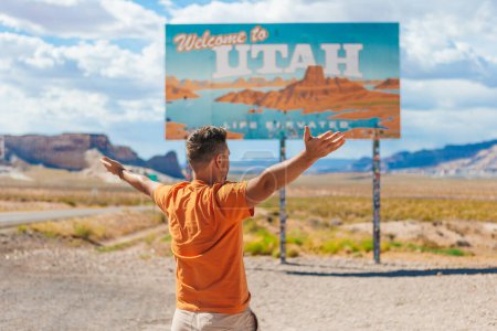 Glücklicher Mann auf USA-Reise vor dem Hintergrund des Willkommen in Utah State Grenzschildes mitten im National Canyon, USA