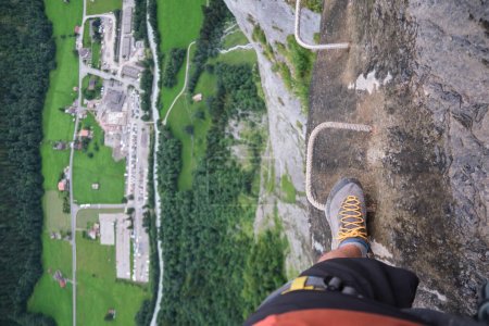 Touristen steigen auf metallene Klettersteige, am Rande einer Felswand, mit riesigem vertikalen Spalt unter ihm und Blick auf das darunter liegende Tal. Sommeraktivität am Murren-Gimmelwald klettersteig, Schweiz