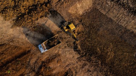 Aerial view of a wheel loader excavator with a backhoe loading sand onto a heavy earthmover at a construction site.