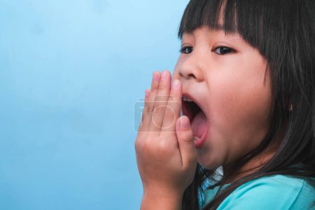 Kleine asiatische Mädchen bedecken ihren Mund, um Mundgeruch zu riechen. Kindermädchen prüft mit ihren Händen den Atem. Mundgesundheit oder zahnärztliches Versorgungskonzept.