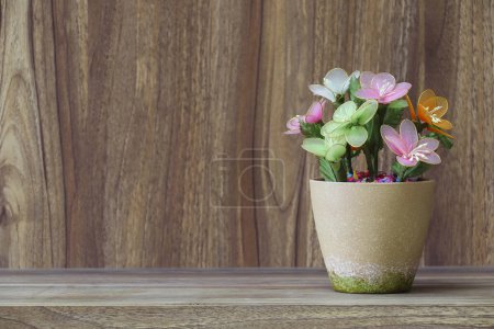 Foto de Flores falsas en un jarrón colocado en una mesa sobre una mesa de madera con espacio de copia para el diseño de fondo vintage de grano de madera. - Imagen libre de derechos