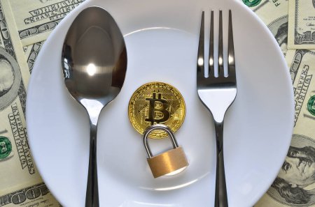 Photo for Bitcoin cryptocurrency, cutlery and lock on a plate among dollars. - Royalty Free Image