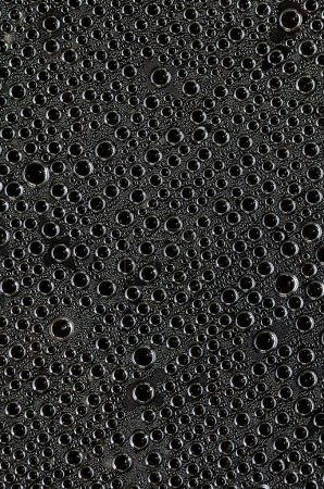 Grandes gotas de agua en una superficie oscura de cerca