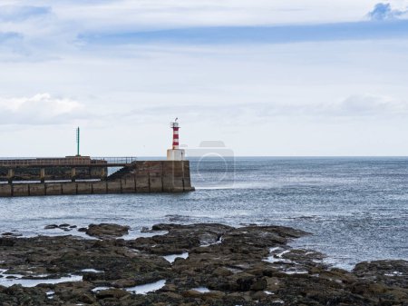 Lighthouse at the entrance to Amble harbour and rocks.