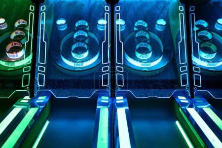 A close up photo on a skee-ball game at a video arcade lit up with blue and green neon lights.