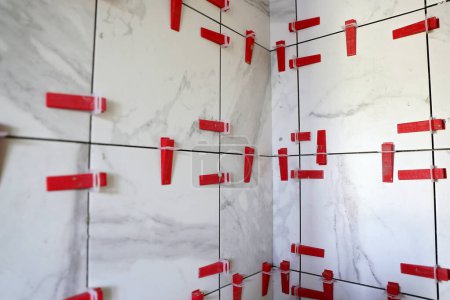 A wall of tile work is being done on a shower and red leveling spacers are dividing the tiles.
