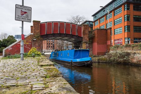 Téléchargez les photos : A blue narrow boat passes under the pretty red Kitty footbridge in the Ancoats area of Manchester in 2023. - en image libre de droit